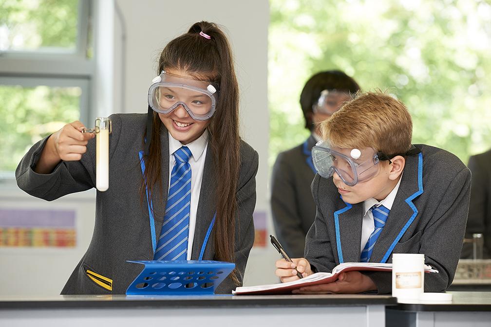 Two students in chemistry class wearing goggles smiling with a test tube doing an experiment.