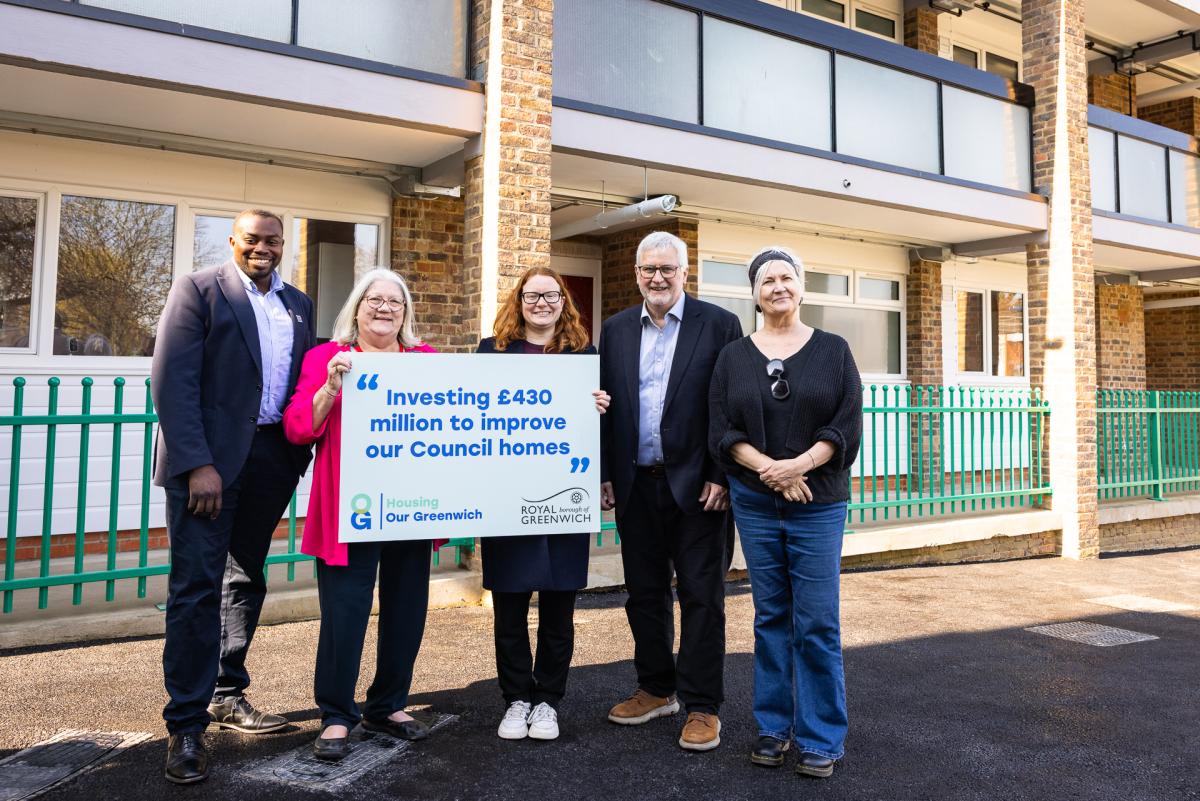 Councillors and local MP gather outside a refurbed block with a sign that reads: "Investing £430 million to improve our council homes".