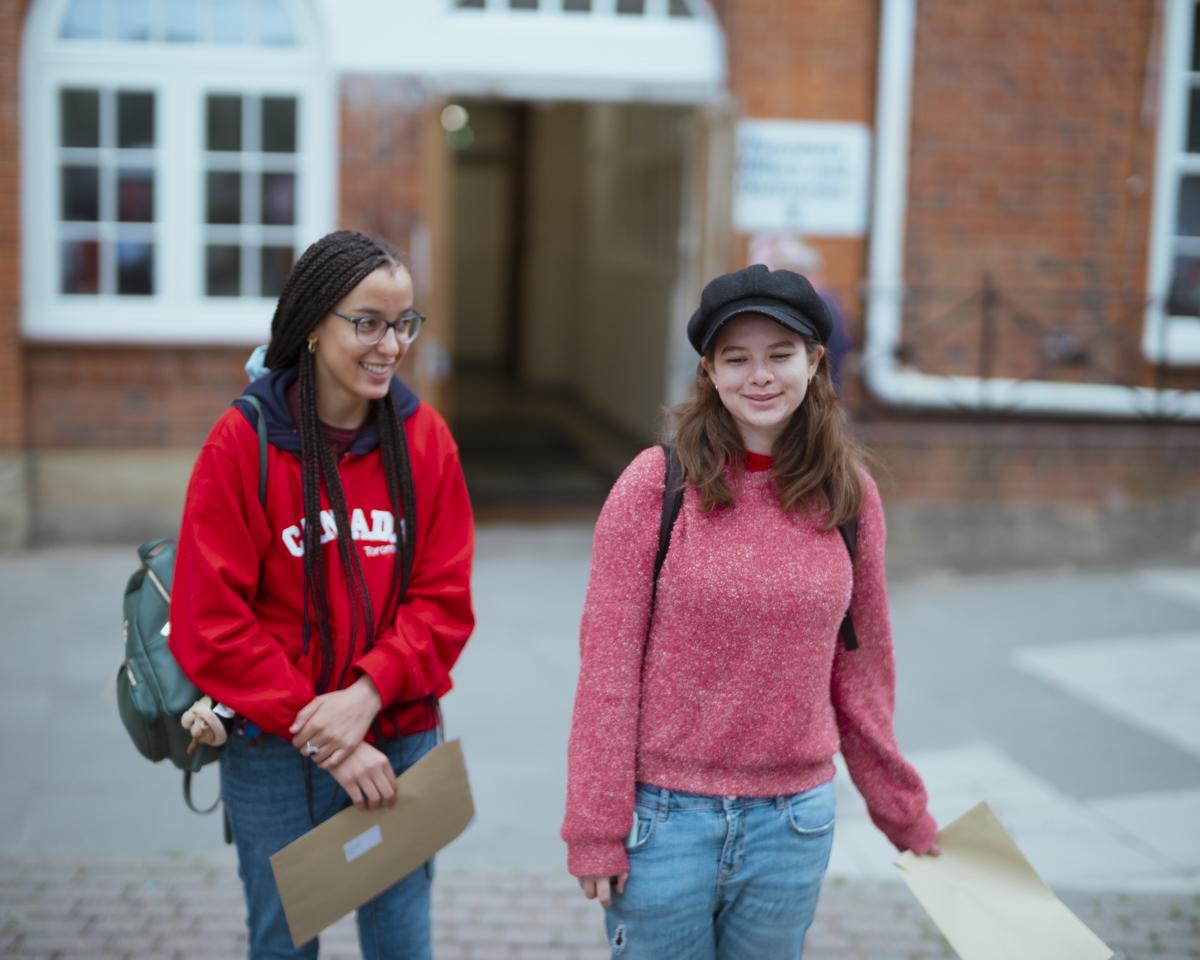 Two students in a school playground wearing a pink and a red sweater, smiling happily.