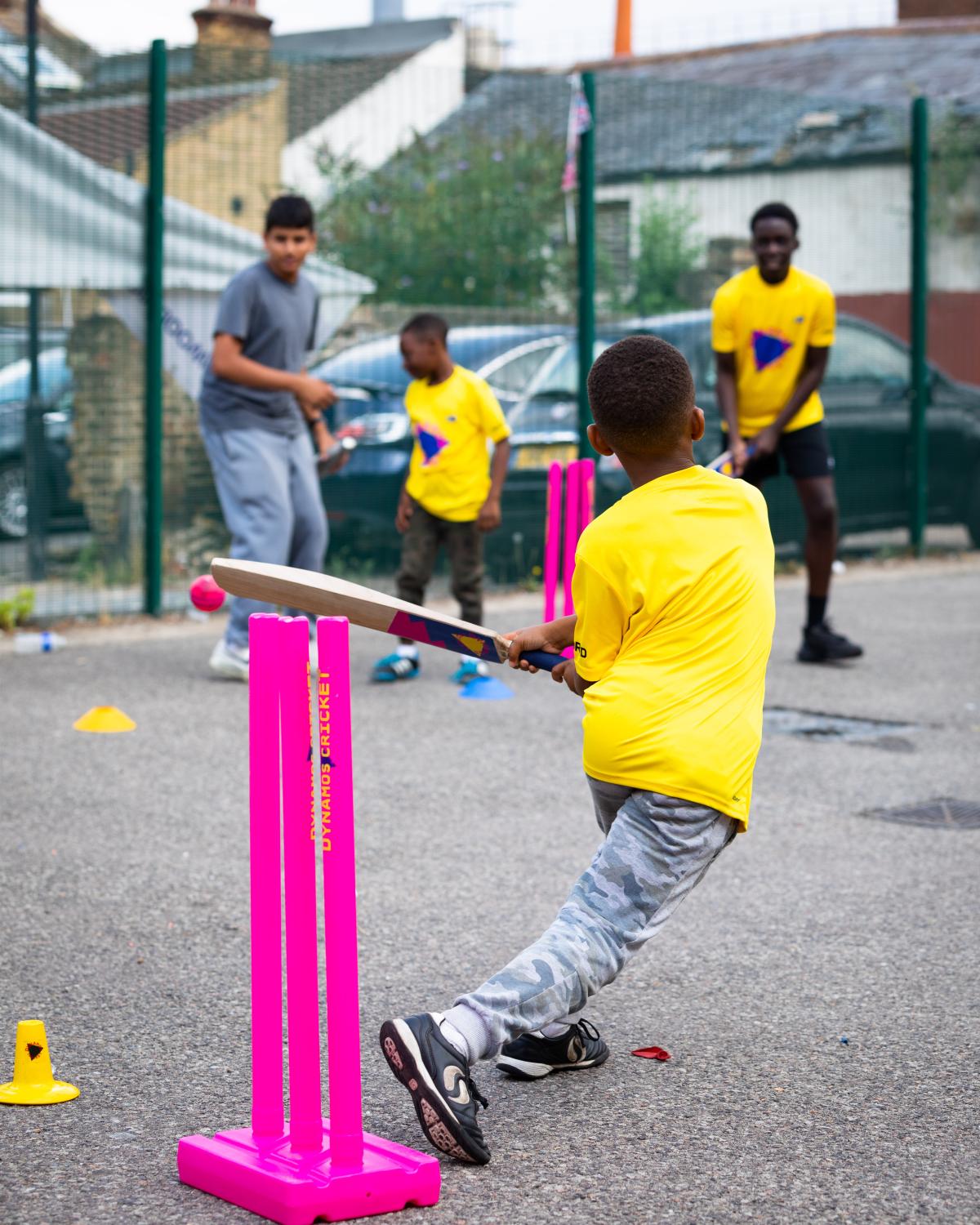 Young boy playing cricket outdoors wearing a yellow t shirt
