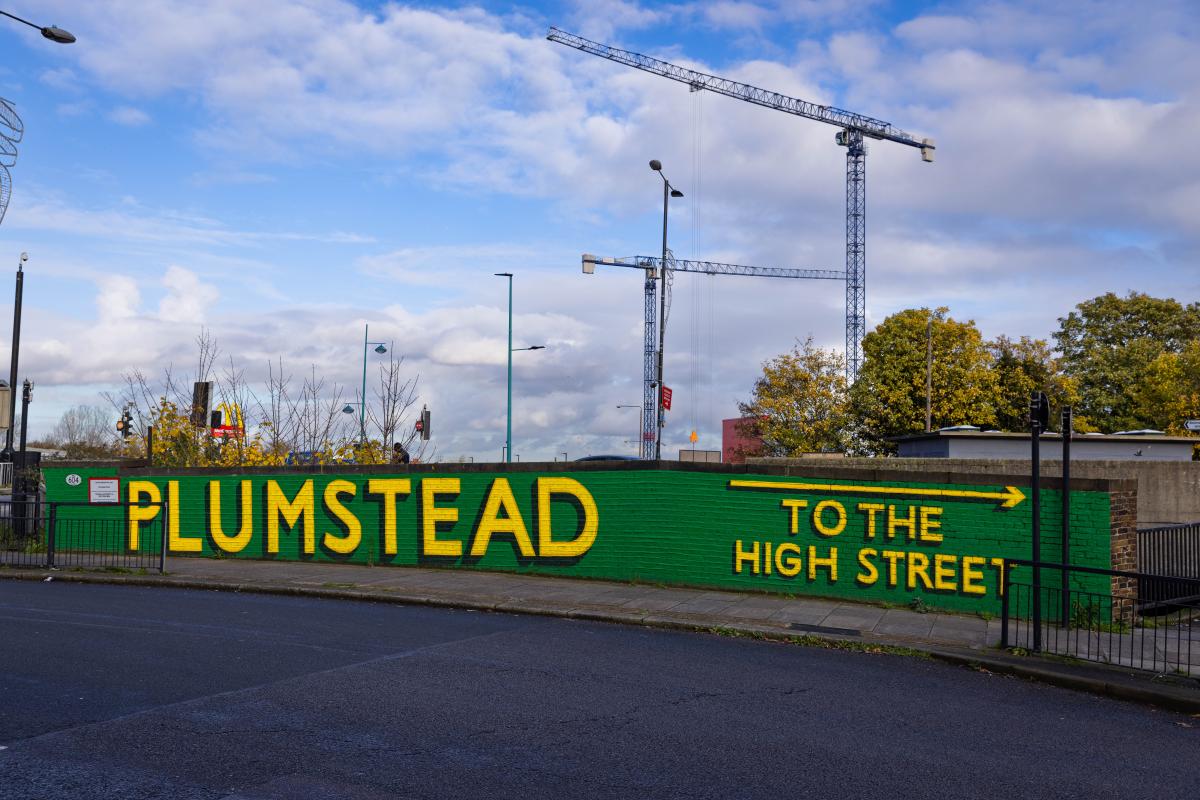 A railway bridge reading 'Plumstead' and 'to the high street'