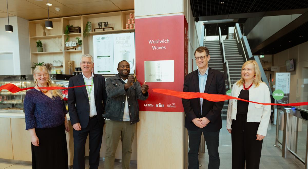Five people stand in a row in front of a plaque that reads 'Woolwcih Waves'. On person is cutting through a red ribbon held up in front of them.