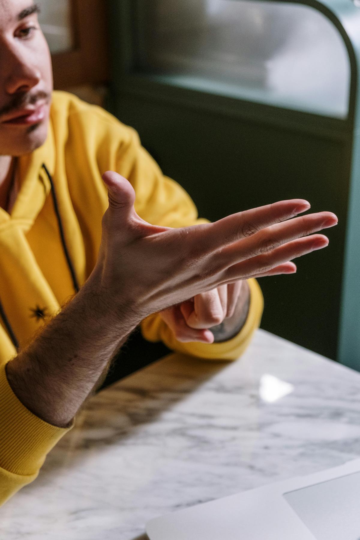 man sitting at table with a yellow top and using his hands to sign