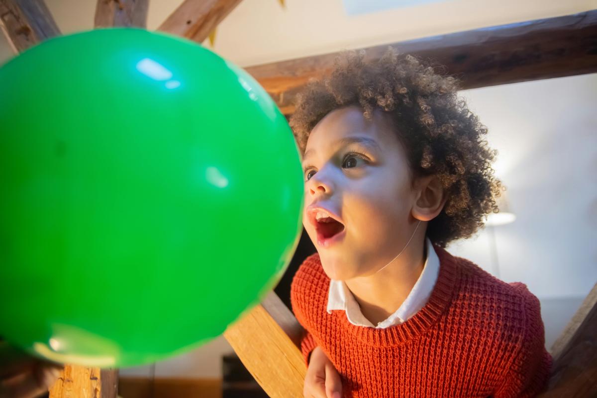 boy around 8 years old with his face close to a large green balloon that is floating