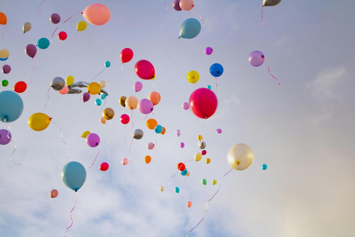 different colour balloons floating up into the sky with white clouds in view