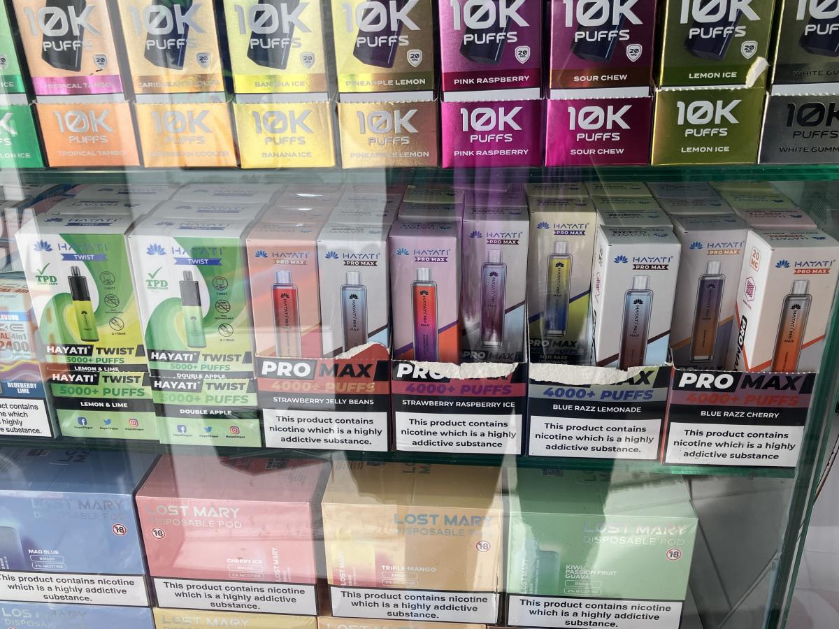 Multiple boxes of vapes behind a cabinet.