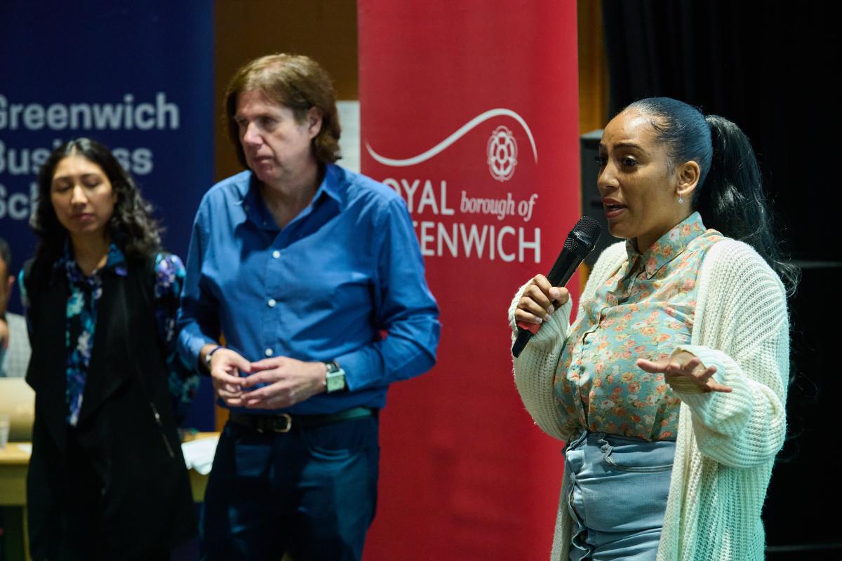 Three people speaking on stage with a red Royal Borough of Greenwich banner behind them. 