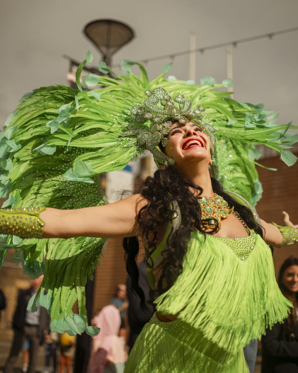A person dressed in bright green carnival clothing, with a feathered head dress on