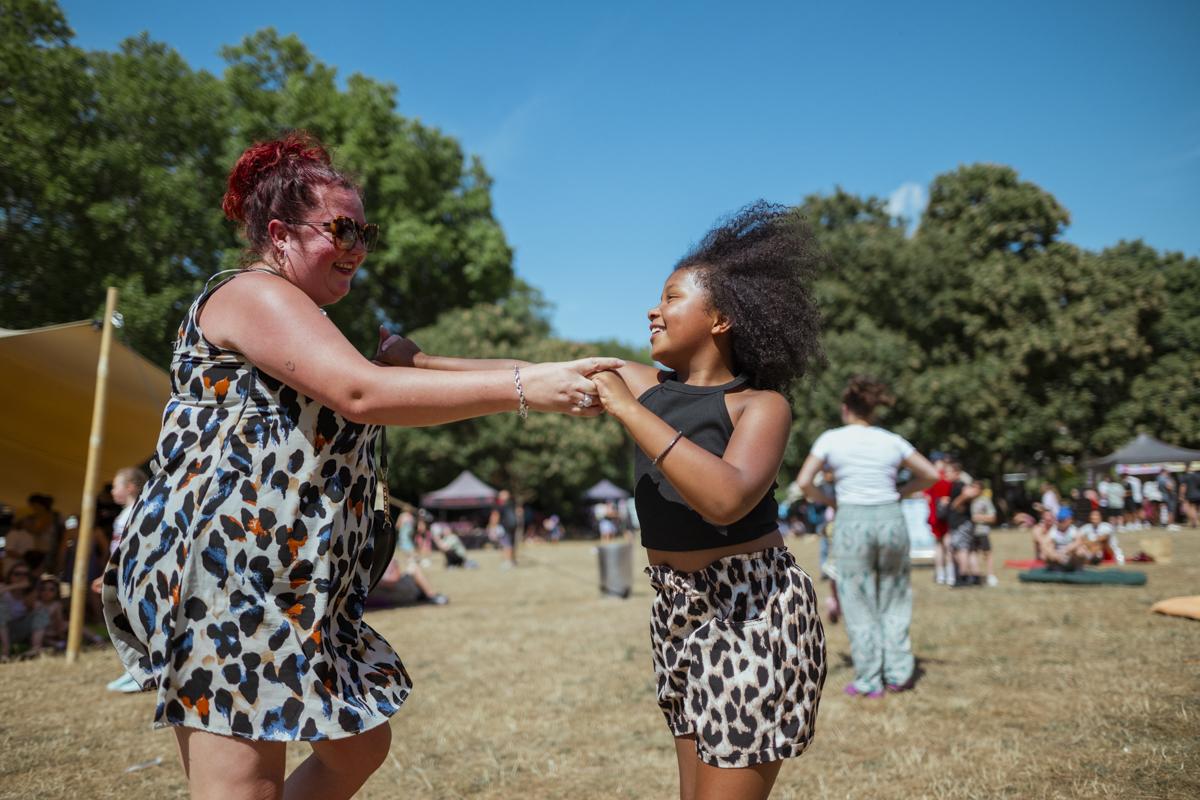 A woman and a child holding hands dancing on grass.
