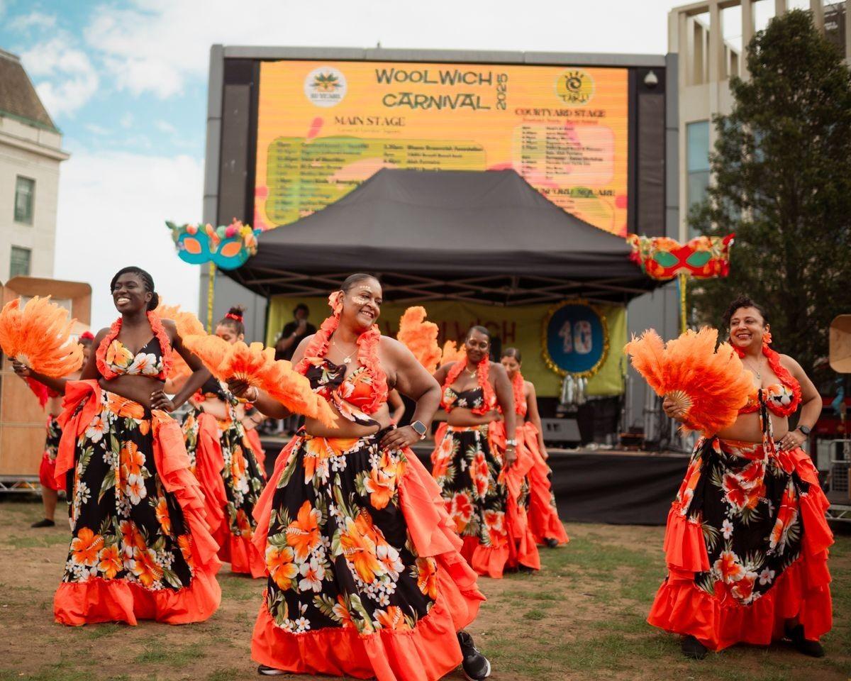 Vibrant dancers in orange‑and‑black costumes performing at Woolwich Carnival 2025.