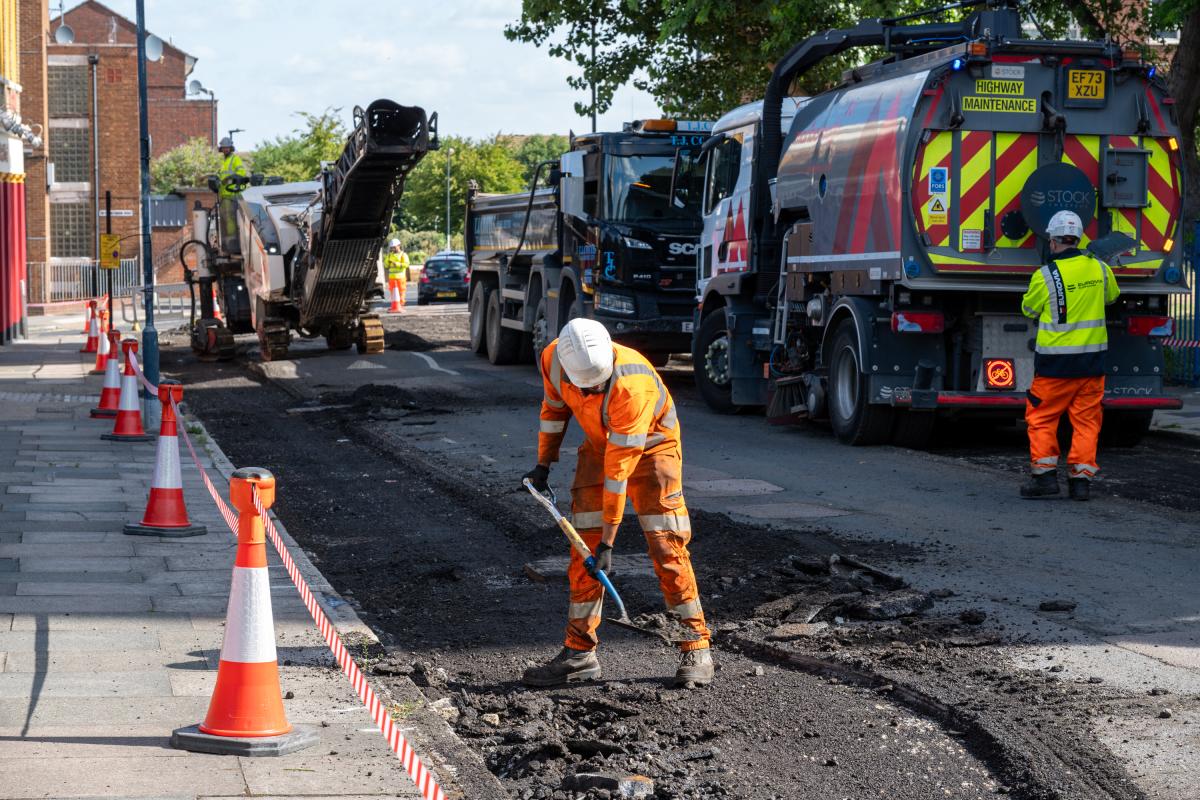A man in an orange hi-vis jacket helping to resurface a road.