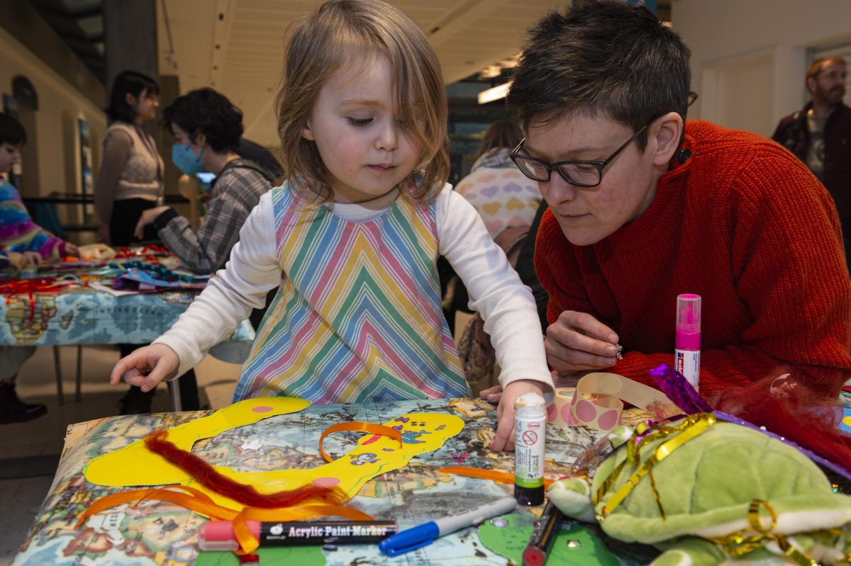 Parent and child getting stuck into Pride themed arts and crafts surrounded by glitter, pritt stick and colourful paper
