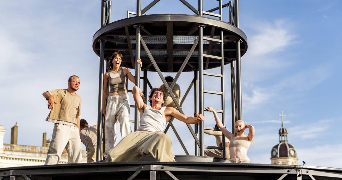 Five people holding onto a circular metal frame. They are dancers about to begin a performance. Behind them blue sky is visible. 