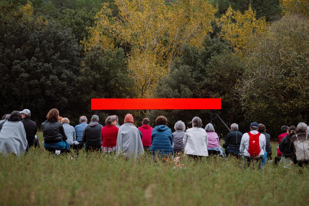 A group of people sat in a field of grass looking towards a stage