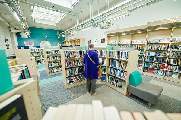 Image of Eltham Library - shelves of books, a woman stands in the middle, with her back to camera