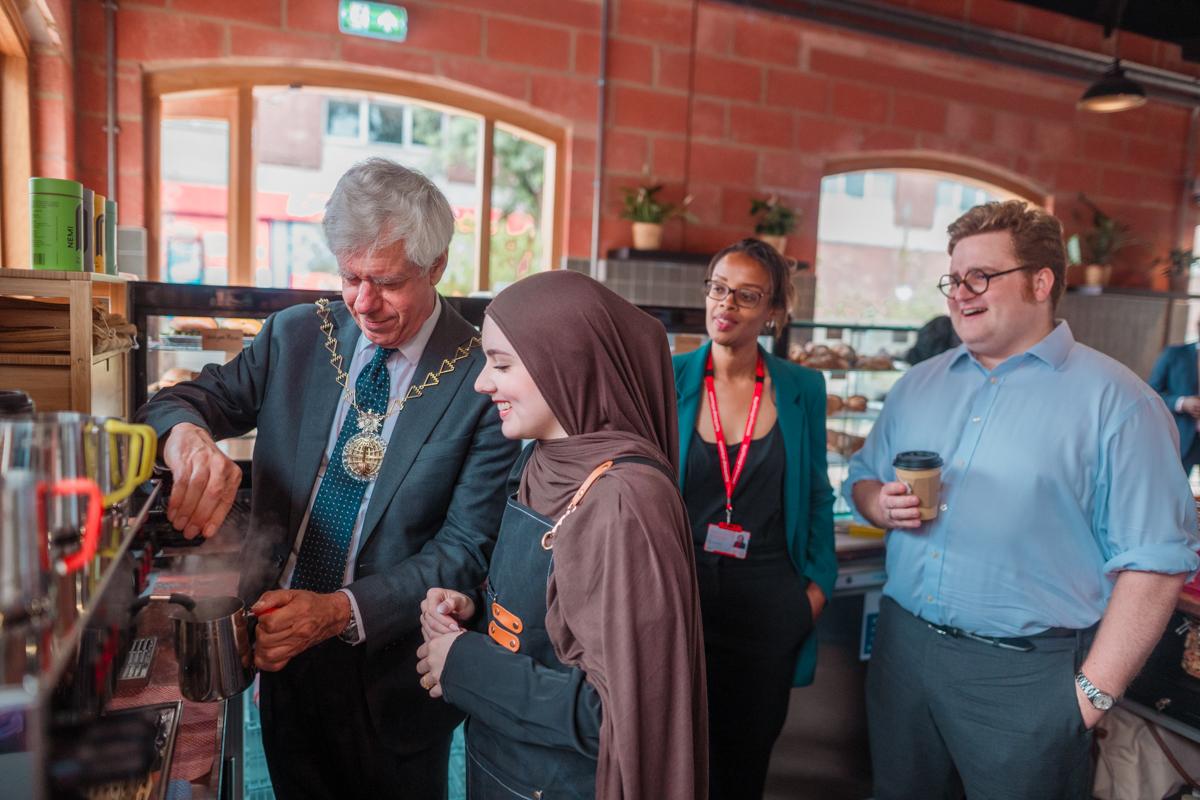 The Mayor of Greenwich (far left) steams milk while making a coffee at the new Bob's Your Uncle cafe in Woolwich