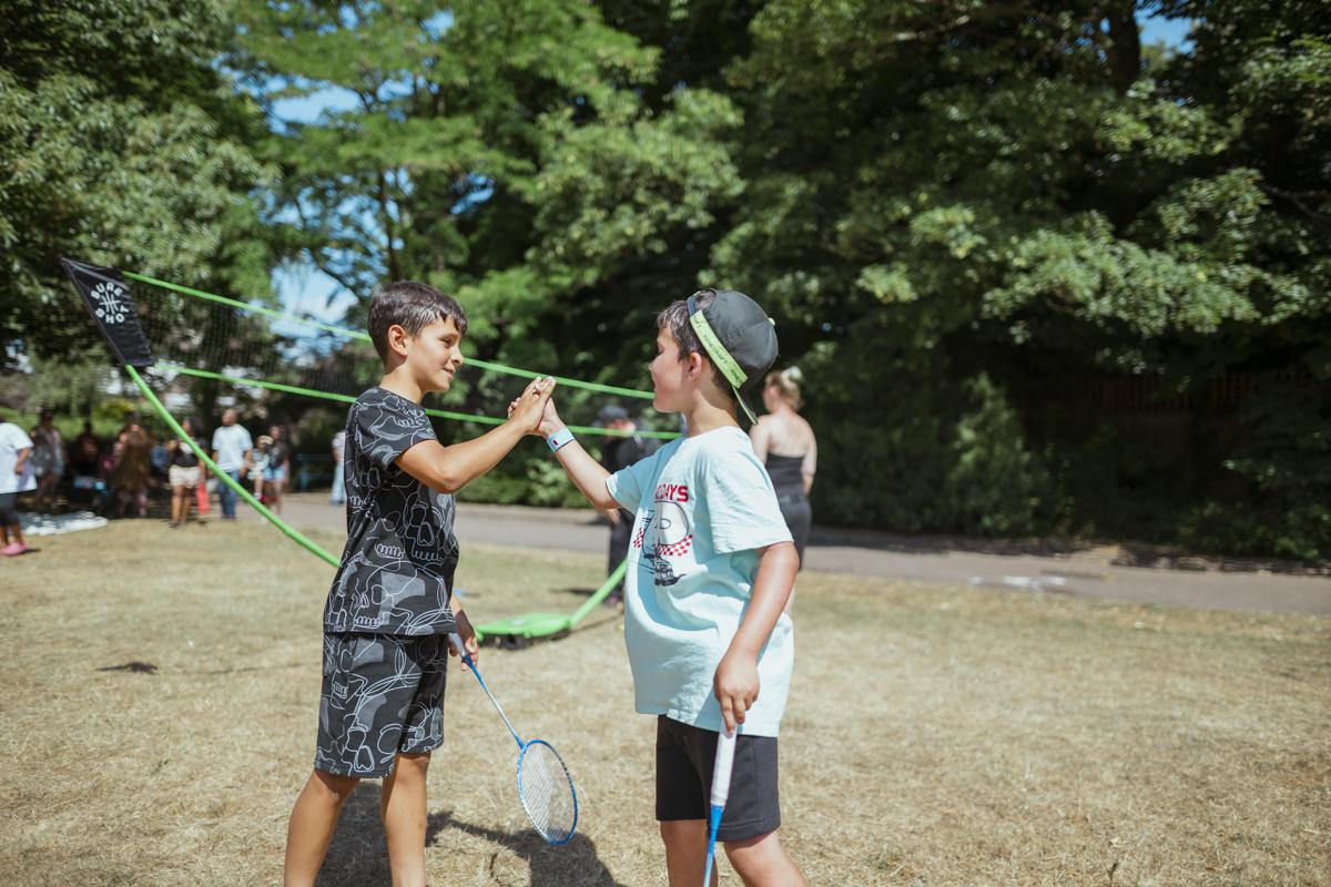 Two children shaking hands on a grass badminton court