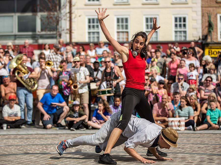 Two dancers performing outdoors in a town centre, in front of a large crowd of people