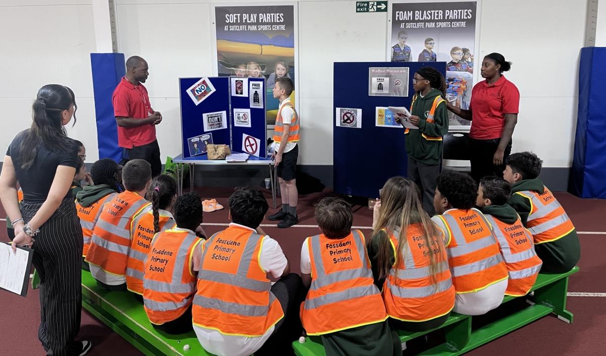 A group of school children are seated listening to a workshop about community safety.