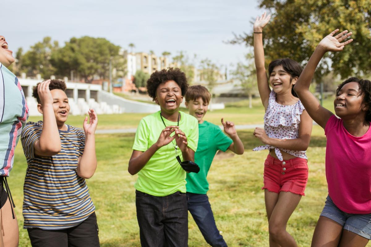 group of 5 teenage children in the park, laughing and waving their hands in the air