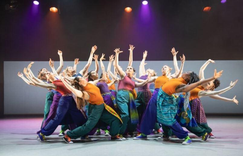 A group of dancers in a huddle with their arms up in the air