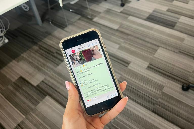 Female hand holding phone unlocked to show Royal Greenwich WhatsApp channel.