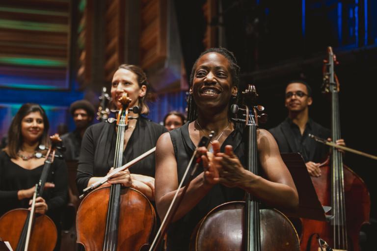 A group of musicians, each holding a string instrument and clapping