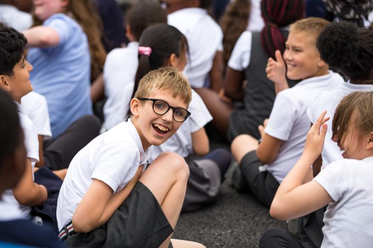 Children sitting down in a playground, one child in glasses is looking directly at the camera smiling.