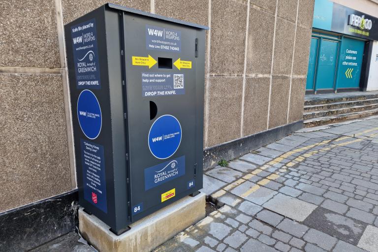 A photo of the knife amnesty bin in Woolwich Town Centre. A grey metal bin installed on a concrete base.