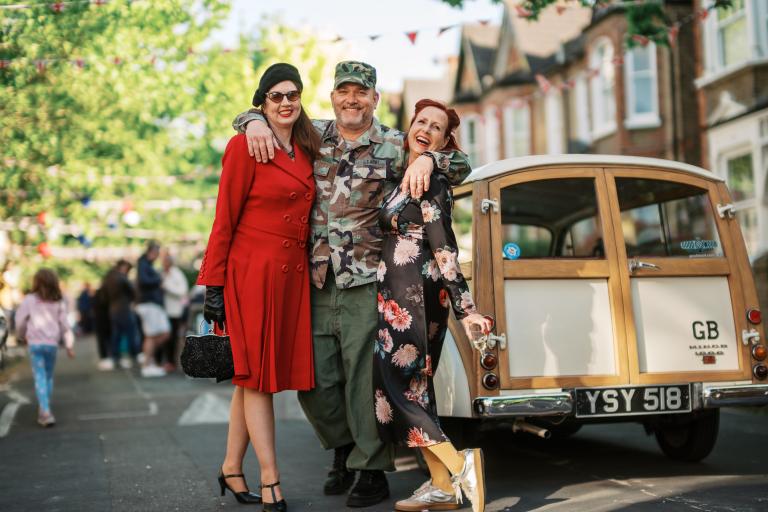 Three people in 40s clothing standing next to a vintage car