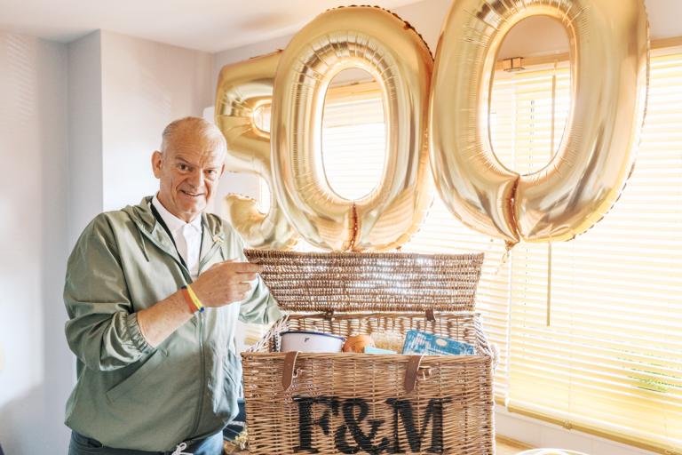 a man stands with a food hamper with the numbers 5-0-0 in golden balloons in the background