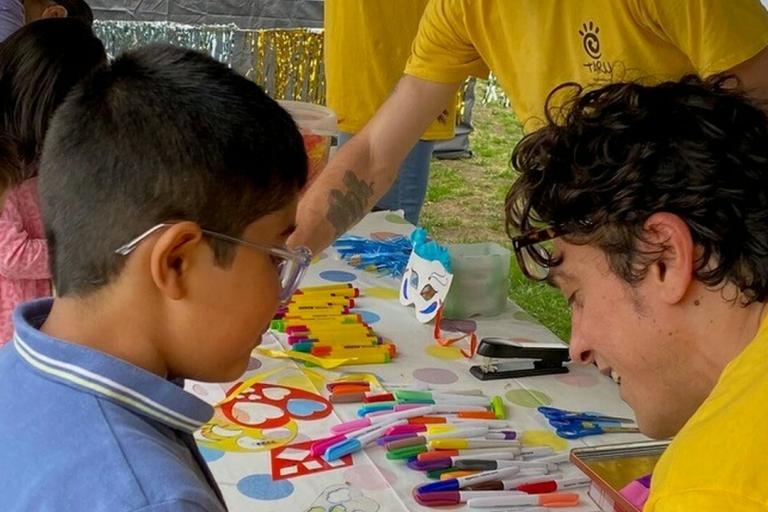 A group of adults in yellow tops helping young children to do arts and crafts at a table.