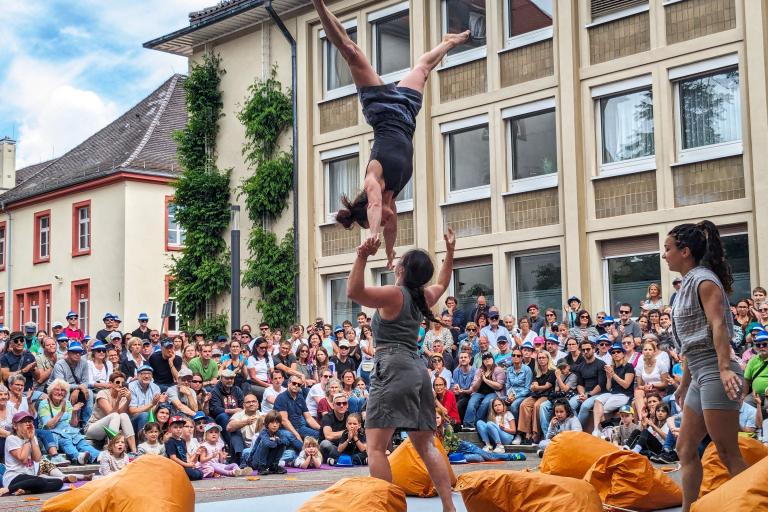 Acrobats perform for a large crowd of people in front of a three story building