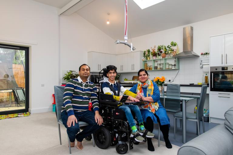two parents and their young son who is a wheelchair in their kitchen. A ceiling height host is shown above the family.
