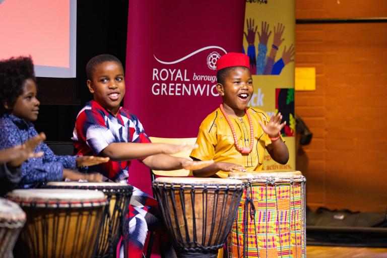 Three children playing drums, they are smiling and look happy