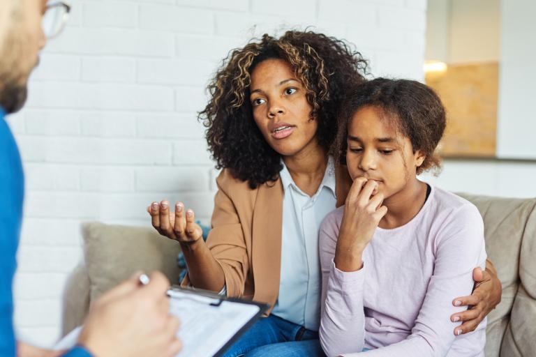 A concerned woman holding her daughter as she speaks to a man with a clipboard.