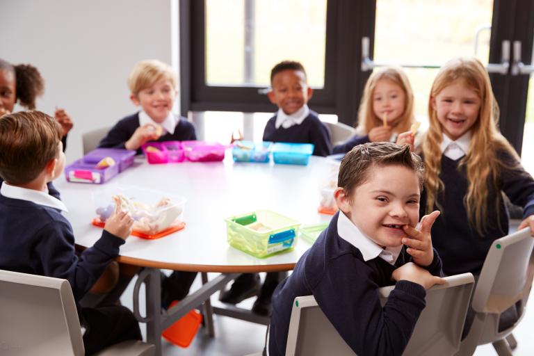 A table of students sitting down with their lunchboxes and smiling at the camera.