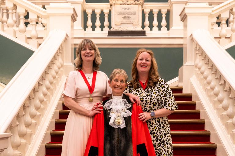 Mayor Cllr Linda Bird in full ceremonial dress standing on the steps of the Woolwich Town Hall with her daughters on either side of her.