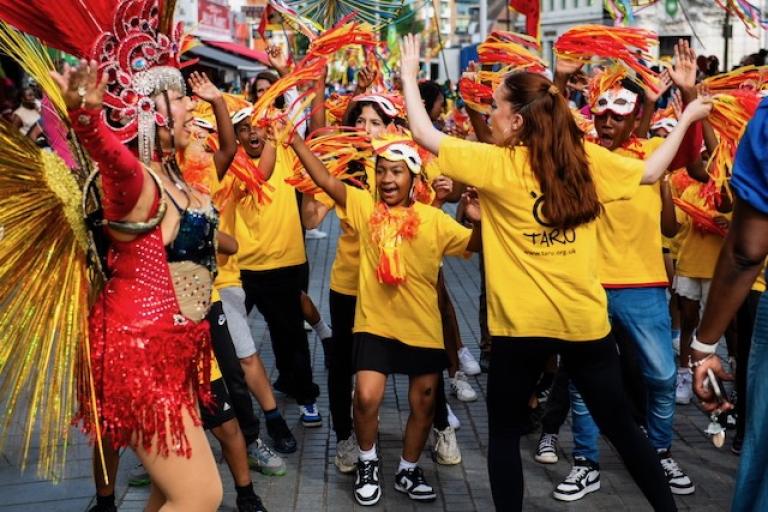 A group of children wearing yellow t shirts and dancing in a carnival parade