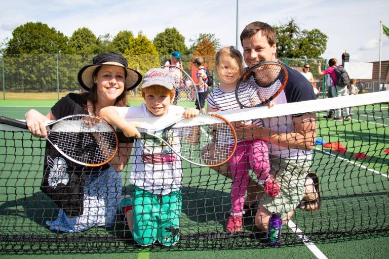 A family of four posing behind a tennis court net.