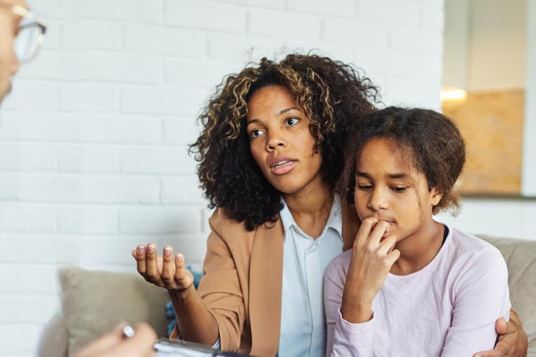 A concerned woman holding her daughter as she speaks to a man with a clipboard.
