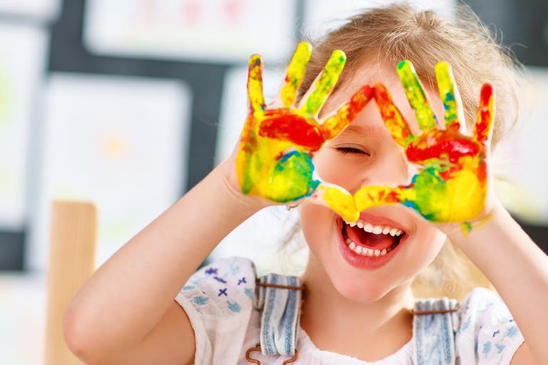 A happy young girl holding up two painted hands.