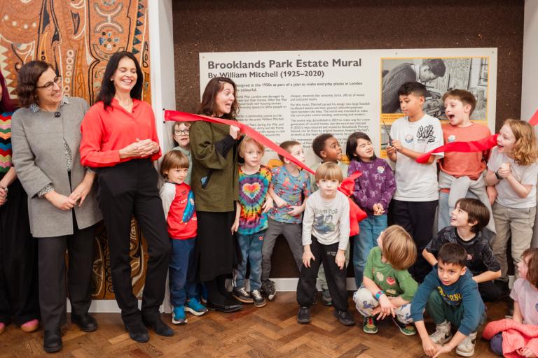 A group of residents, councillors, school pupils and heritage professionals cut a red ribbon in front of the Brooklands Mural.