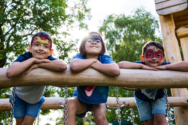Three children with painted faces smiling on a climbing frame