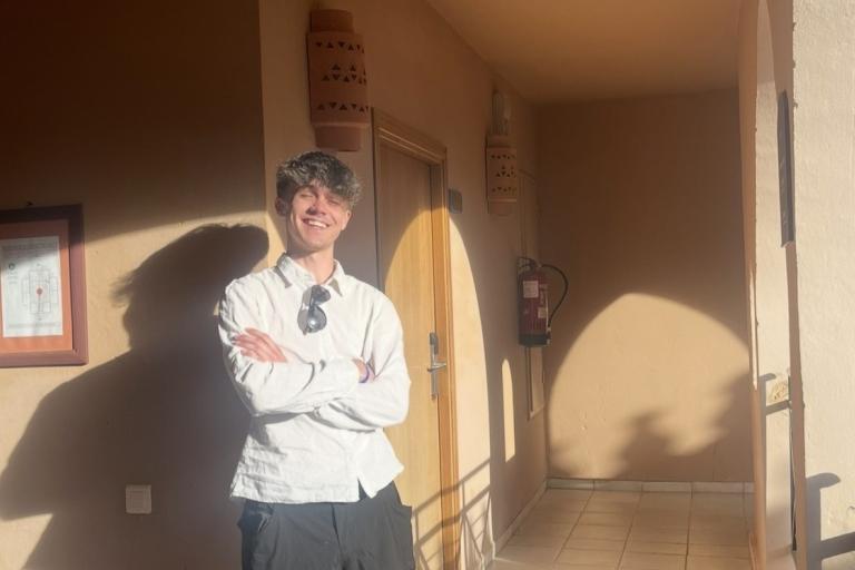 Young person standing with a big smile and arms crossed on a sunny balcony