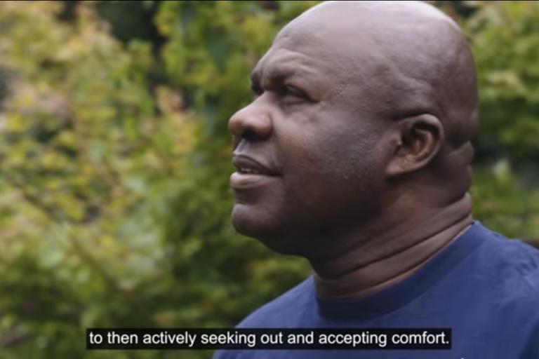 Man looking into the horizon speaking about experience fostering, the background features greenery like in a garden.