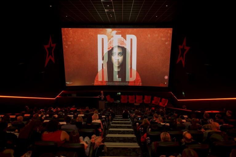 Inside a cinema screening, the film poster for Red is on the screen