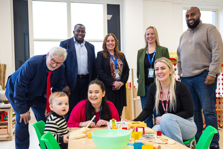 A photo of Clive Efford MP, Leader of the Royal Borough of Greenwich Cllr Anthony Okereke, Cabinet Member for Children and Young People Cllr Adel Khaireh smile with staff and children at More2Kidbrooke nursery in Kidbrooke.