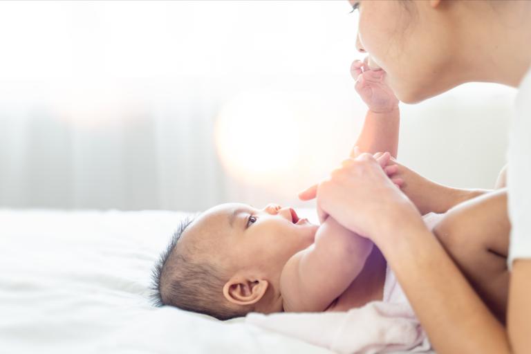 A newborn baby laying down with their parent kissing their foot.