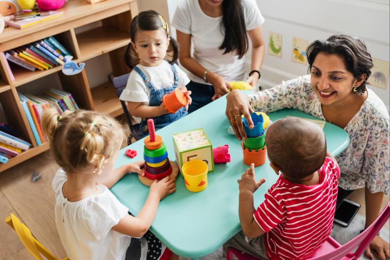 Three young children sitting at a table next to two adults as they play various toys.